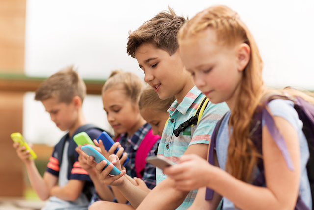 This is a picture of kids using smartphones.  Prolonged computer and smartphone usage can lead to bad posture where the head and shoulders are draw forward called tech neck.  This article is about how to fix tech neck.