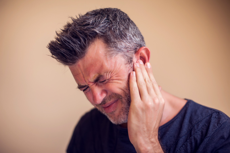 This is a picture of man holding his ear in discomfort because of tinnitus. Chiropractic for tinnitus is a safe and drug-free treatment option.