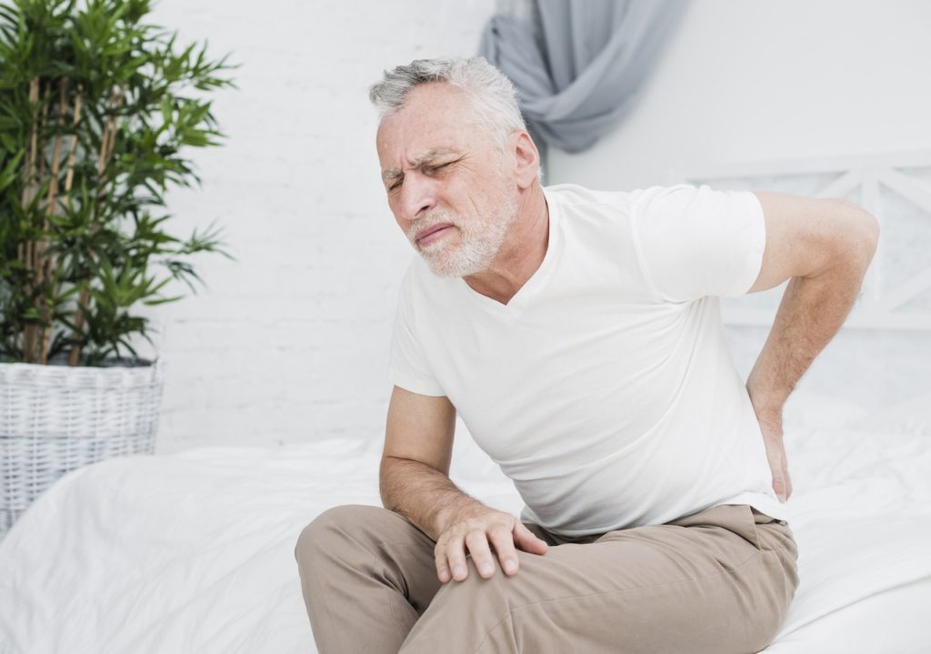 This is a picture of a man bent over in his bed in pain holding his lower back. the picture depicts a man where his sciatica won't go away.
