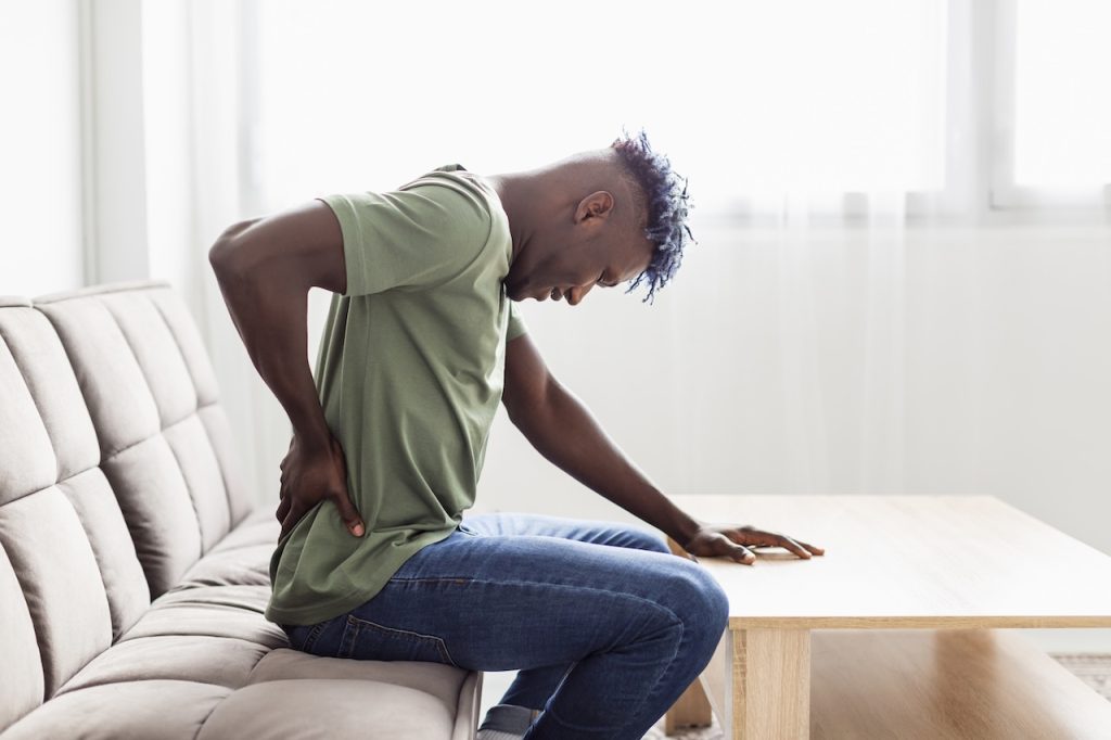 This is a picture of a man sitting on a couch struggling with sciatica. The picture helps depict the main them of the blog post - what causes sciatica.