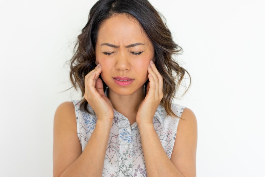 This is a picture of a woman holding her jaw in pain with headache. It depicts the title of the post, 'Can TMJ Cause Headaches?'