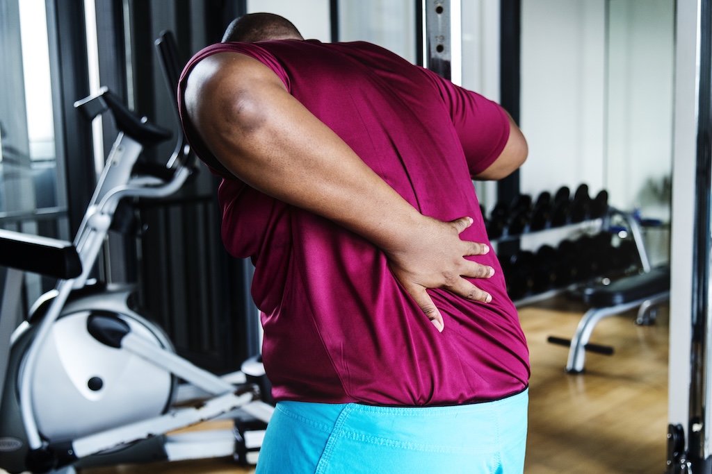 Person experiencing lower back pain after working out at a gym in Edmonton