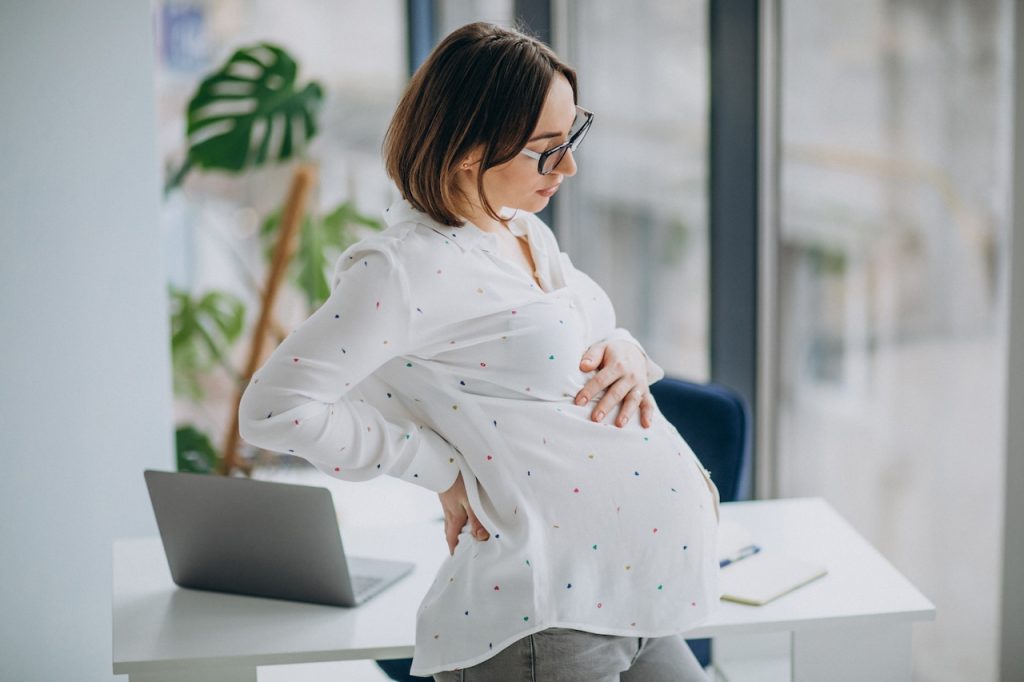 This is a phot of a pregnant woman with back pain and it depicts what the post is about, 'Why Does My Back Hurt During Pregnancy?'