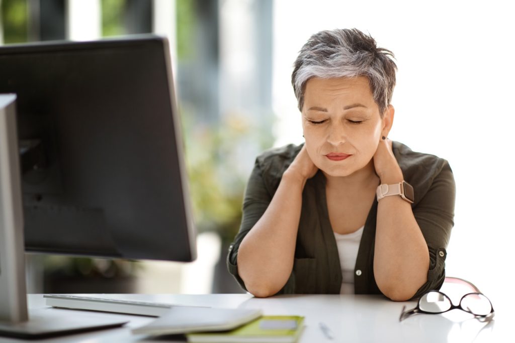Woman noticing neck stiffness while working at a computer